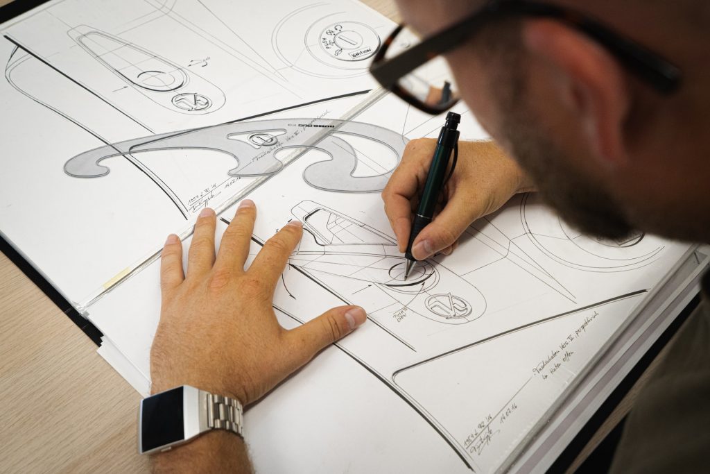 Industrial designs, image of a draftsperson drawing what looks like parts of a car, taken from over the shoulder