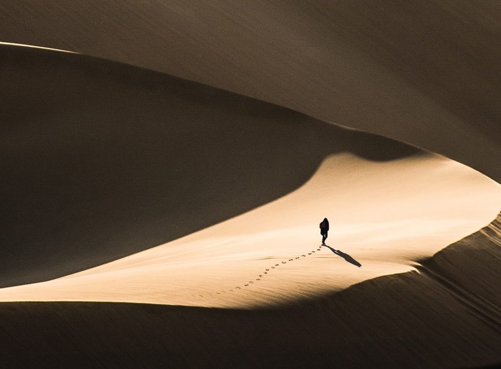 Image of a man lost in the desert, you can see sillhouettes of dunes.