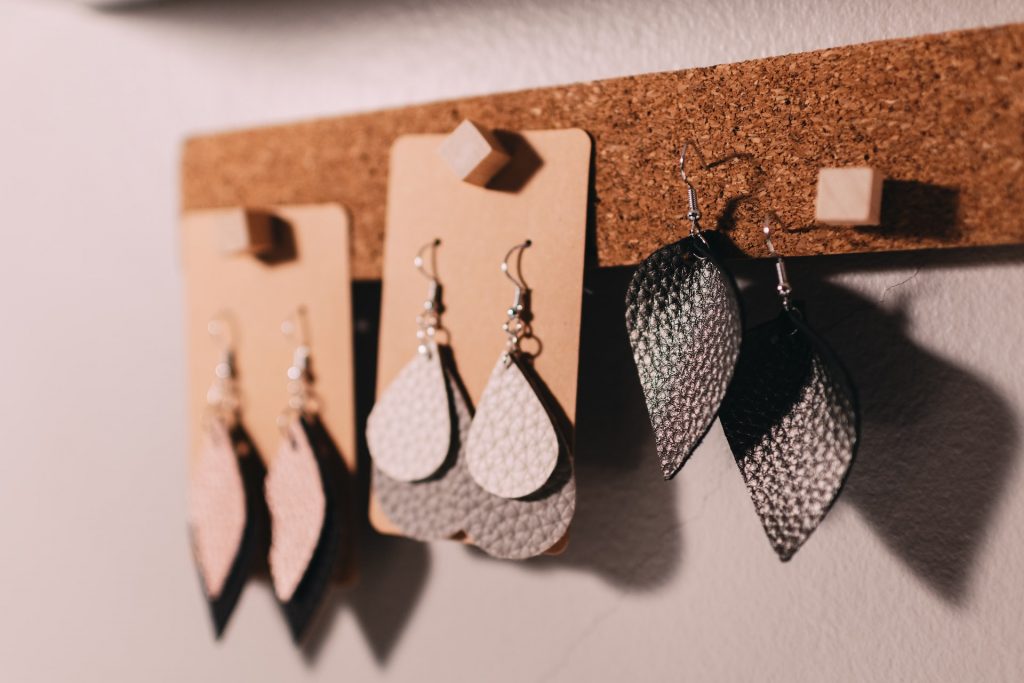 Image of a set of handcrafted earrings hanging off metal hooks, fastened to a wooden board on the wall