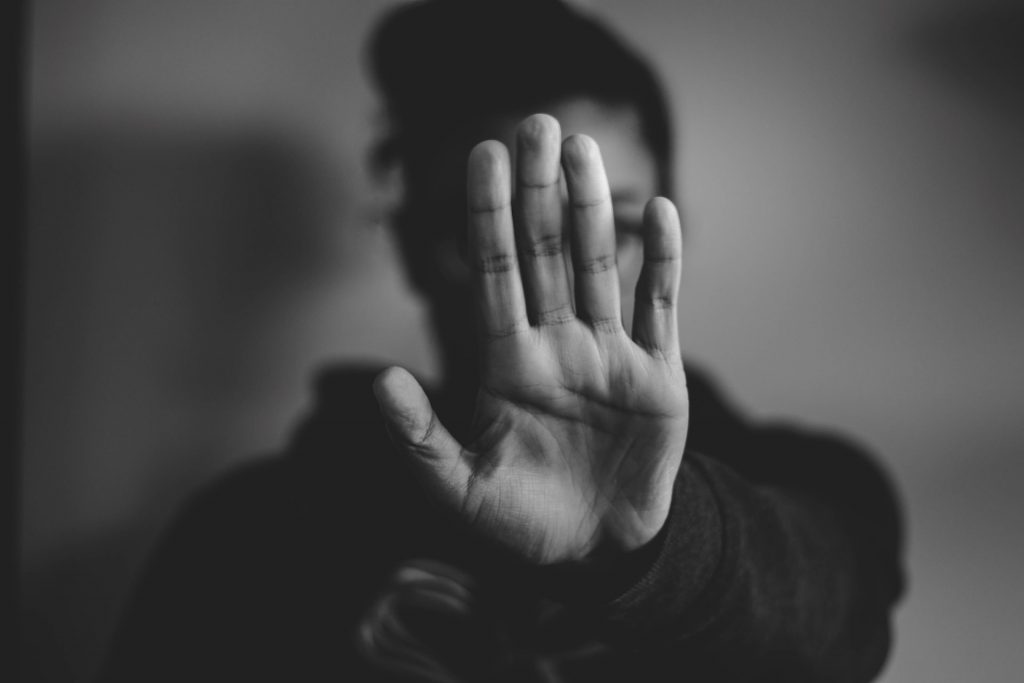 Black and white image of a person raising their palm to the viewer and obscuring their face.